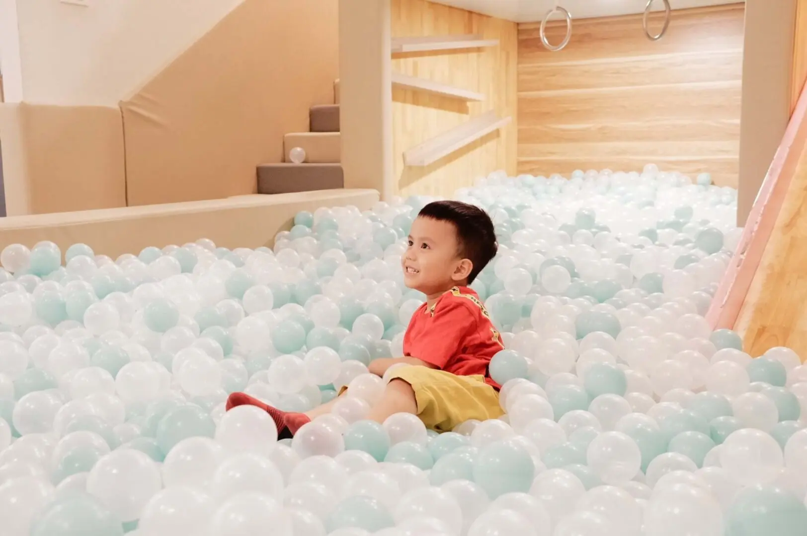 A young boy sitting in the middle of a room filled with white balls.